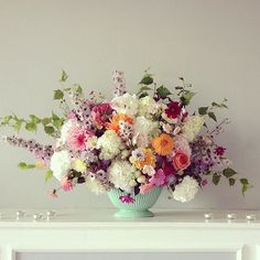 a vase filled with lots of colorful flowers on top of a white table next to a fireplace