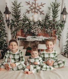 three children in matching pajamas sitting on a bed with christmas decorations and snowflakes