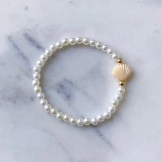 The Shelly Bracelet is here!  Featuring a single Clam Shell in your choice of color on a pearl beaded band paired with a Gold filled hug, finished with our Laguna brand tag. Clam Shell Color Options:  Mint Blue  Purple White Yellow Peach Pink Tan Please measure before you order! Sizing can vary by age.  Bracelets are made with a durable stretch elastic to comfortably slide on and off your wrist. Size Chart: XXS- 5.5" XS- 6" Small- 6.5" Medium- 7" Large- 7.5" XL- 8" Sizing details: To measure wrist grab a string or paper wrap it tightly around wrist in place desired. Then Measure string against ruler add 1/2" to size as beads will tighten the fit once on string.  If you are in between sizes, I would recommend sizing down since they do stretch. Gift wrapping and packaging: All orders come in Pearl And Shell Bracelet, Adjustable Pearl Bracelet With Charm And Round Beads, Adjustable Pearl Beaded Bracelets With Pearl Drop, Pearl White Adjustable Pearl Charm Bracelet, Adjustable Pearl White Beaded Bracelets With Pearl Drop, Adjustable Beaded Pearl Bracelet With Pearl Charm, Adjustable Beaded Pearl Bracelets With Pearl Charm, Adjustable Hand-strung Pearl White Pearl Bracelet, Adjustable Hand-strung White Pearl Bracelet