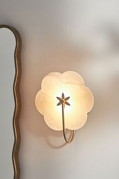 a white flower shaped light on the wall next to a mirror that is reflecting it's image