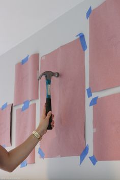 a person holding a hammer in front of pink sticky notes on a wall with blue tape