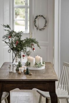 a table with candles and greenery on it in front of a wreath hanging from the wall