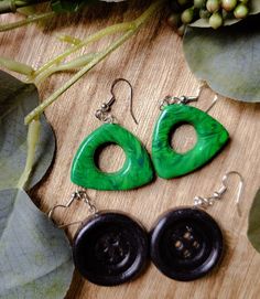 two pairs of green and black earrings sitting on top of a wooden table next to leaves