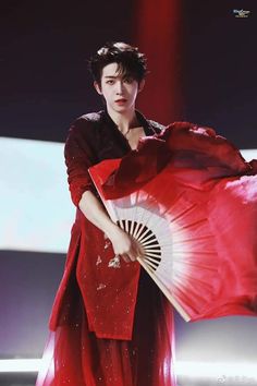 a woman in a red dress holding a fan and posing for the camera on stage