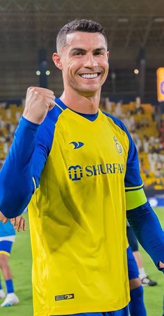 a man in a yellow and blue soccer uniform holding his fist up while standing on a field