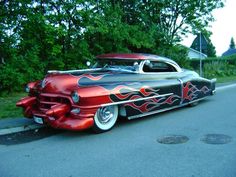 an old car with flames painted on it's hood is parked in the street