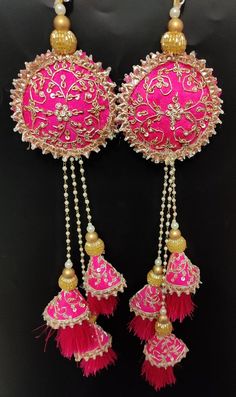 two pink and gold earrings with tassels hanging from the side on a black background