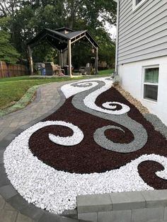 an outdoor walkway with gravel and rocks in the shape of swirls on it, leading up to a house