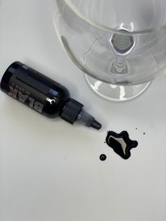 a bottle of black ink sitting next to a glass filled with liquid on top of a table