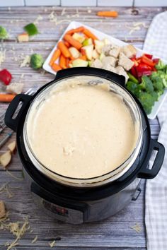 a pot filled with soup sitting on top of a wooden table next to vegetables and meat