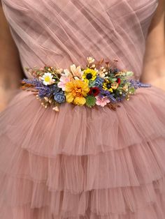 a woman wearing a pink dress with flowers on the waist and in the back, there is a belt made of tulle