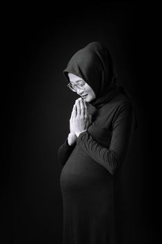 a woman wearing a hoodie and holding her hands to her chest while standing in front of a black background