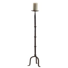 a tall metal candle holder with a single white candle on it's end and an iron stand