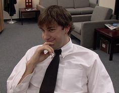 a man wearing a white shirt and black tie sitting in an office with his hand on his chin