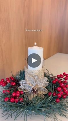 a white candle sitting on top of a table next to red berries and pine cones