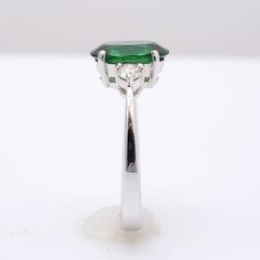 This oval cut Tsavorite Garnet, set at the center of this ring steals the show. It’s rich green, has been highlighted by the perfectly matched round brilliant diamonds that rest on either side of the center stone. Eye clean and large in size, this 2.13 carat stone is a rare gem. Set in 18K white gold, this ring is just the right combination grace and beauty. Order online info@jupitergem.com Oval Tsavorite Diamond Ring For Formal Occasions, Brilliant Cut Oval Diamond Ring With Tsavorite, Gia Certified Oval Green Diamond Ring, Green Oval Diamond Ring Fine Jewelry, Oval Tsavorite White Gold Ring, Oval Tsavorite Ring In White Gold, Oval Tsavorite Ring With Center Stone, Oval Tsavorite Rings With Halo Setting, Green Oval Diamond Ring