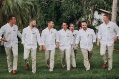 a group of men walking across a lush green field next to each other in white shirts and khaki pants