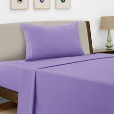 a bed with purple sheets and pillows on top of it in a room next to two pictures