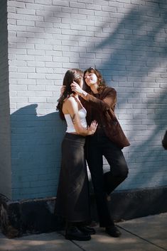 two women standing next to each other in front of a brick wall with their arms around each other