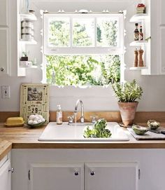 a kitchen with white cabinets and wooden counter tops, an open window above the sink