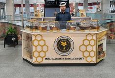 a man standing behind a counter with honey jars on it's display case in an airport