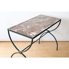 a table with a marble top and metal legs on a wooden floor in front of a white wall