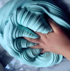 a person's hand touching the top of a blue frosted cake with swirls