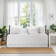 a white day bed sitting in front of a window next to a potted plant