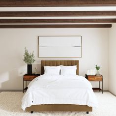 a bed with white sheets and pillows in a bedroom next to a painting on the wall