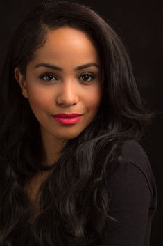 a woman with long black hair and bright red lipstick posing for a photo in front of a black background