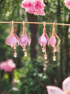 pink earrings hanging from a clothes line with flowers in the foreground and trees in the background