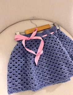 a crocheted blue skirt with pink ribbon tied around the waist on a white chair