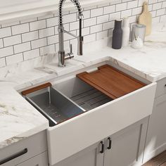 a kitchen sink with a wooden cutting board in the bottom drawer and white countertops