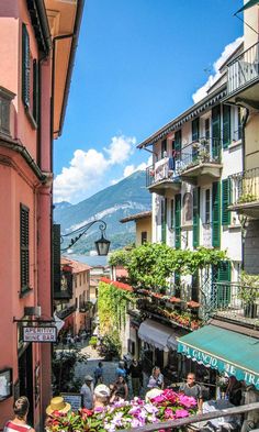 people are walking down an alley way with flowers in the foreground and mountains in the background