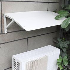 a white air conditioner sitting on top of a wall next to a green plant