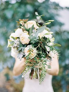 a woman holding a bouquet of white flowers and greenery in front of her face