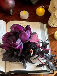 an open book sitting on top of a wooden table next to some candles and flowers