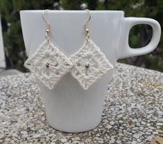 a pair of crocheted earrings sitting on top of a white cup next to a mug