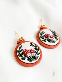 the earrings are decorated with red and green leaves, mushrooms and pine cones on them