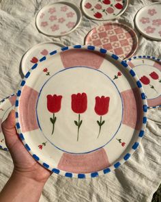 a hand holding a plate with red flowers on it and six plates in the background