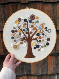 a person holding up a hand embroidered tree with buttons on it