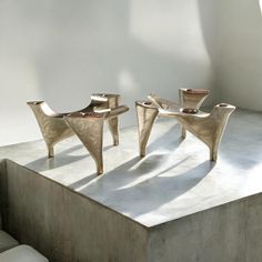 two metal chairs sitting next to each other on top of a cement slab in front of a white wall