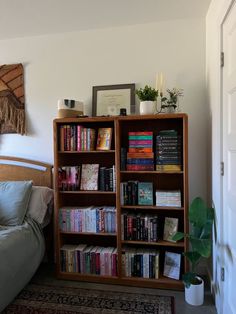 a book shelf filled with lots of books next to a bed and potted plant