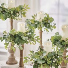 candles and greenery are arranged in vases