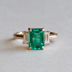 an emerald and diamond ring with three baguets on the side, set in yellow gold