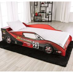 a red race car bed with white pillows and black rugs on the floor in a bedroom