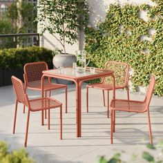 an outdoor table with four chairs and a vase on the ground in front of it