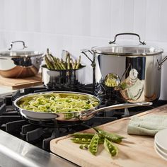 a stove top with pots and pans on it next to green beans, asparagus and other vegetables