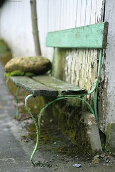 a green bench sitting next to a wooden wall