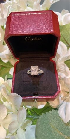 an engagement ring sits in a red box surrounded by flowers